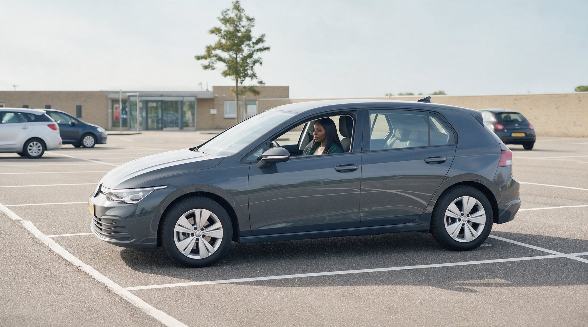 Het parkeerterrein van het examencentrum, de lesauto stil in een vak, de instructrice wacht