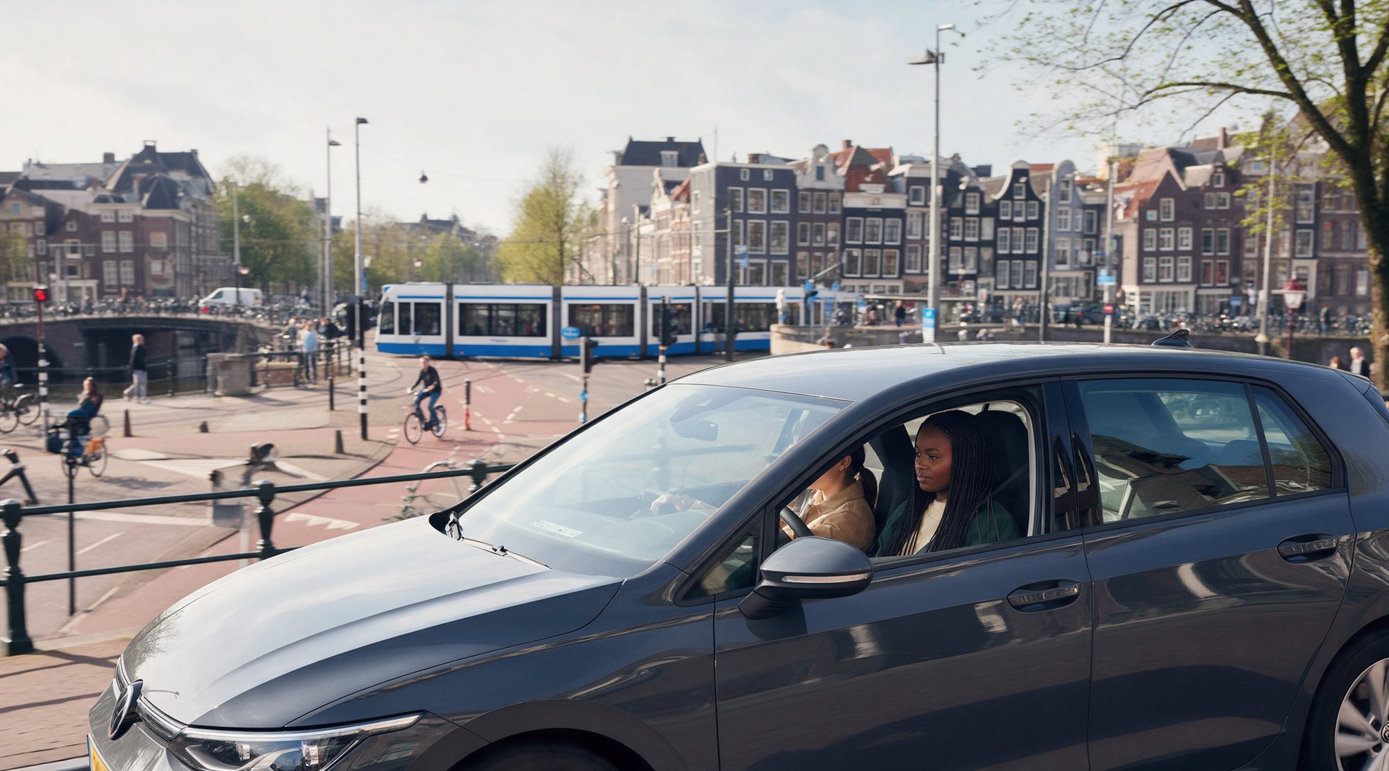 Een drukke stadsstraat met een tram, fietsers op het rode fietspad en de lesauto op de voorgrond