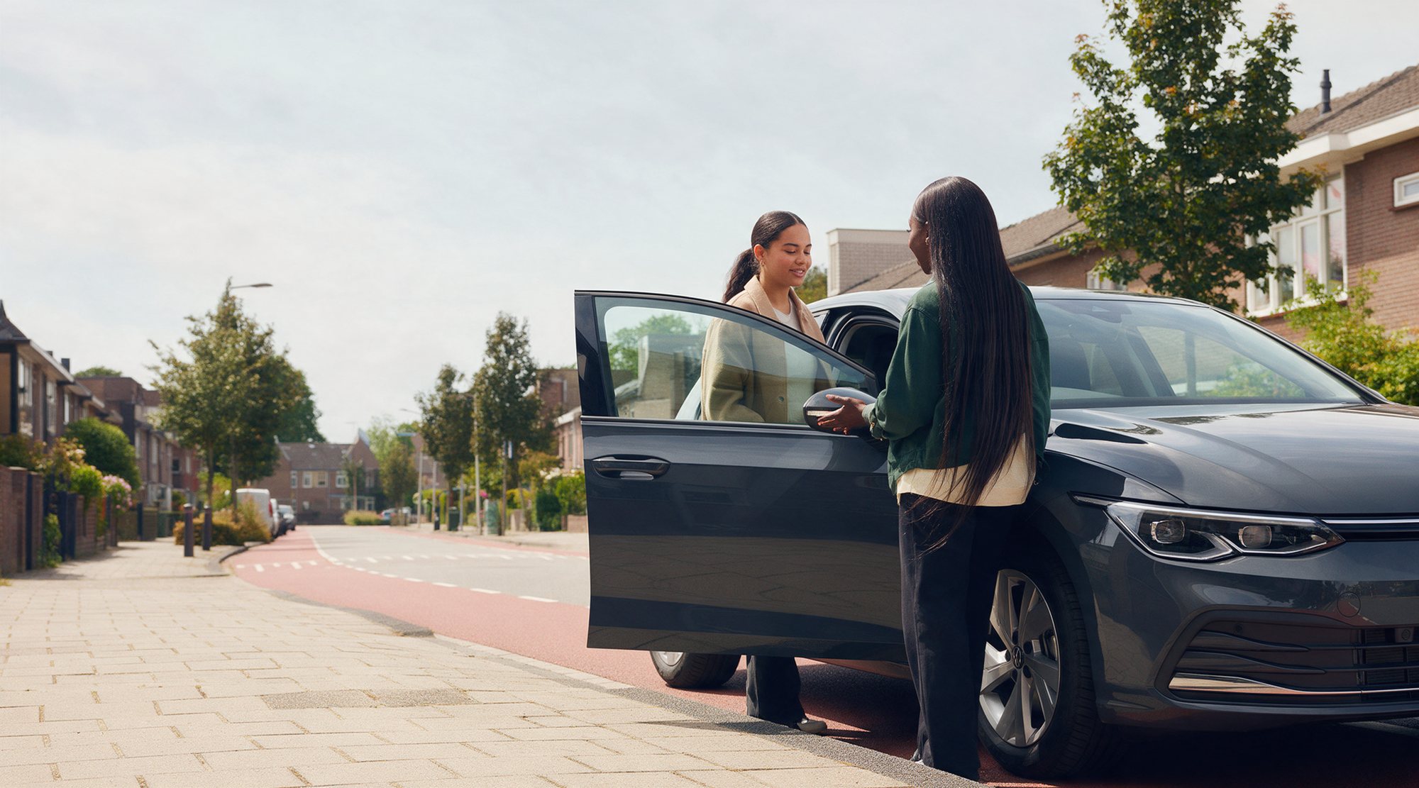 De instructrice begroet de leerling bij de open deur van de lesauto, op een rustige woonstraat